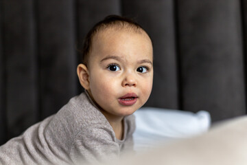 Sweet baby boy on the bed. Just awake toddler. Funny face of chubby child