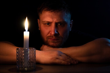 A man sits in the dark with a candle at the table.