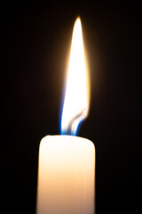 A wax candle burns in the dark.
