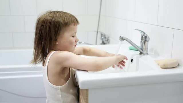 Toddler child turns on the water in the sink in the bathroom, the child himself washes his hands in the bathroom. Hygiene and Toddler Independence