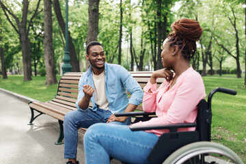 Fototapeta premium Cheery young black woman in wheelchair speaking to her boyfriend at urban park, copy space