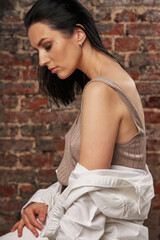 portrait of a beautiful young woman with black smooth hair in a white shirt, in profile, closed her eyes and lowered her head against a brick background