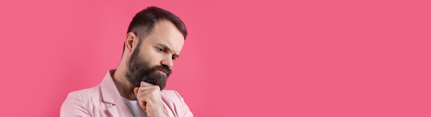 Fototapeta premium Handsome man with a beard in a pink jacket is thinking over an isolated red background.