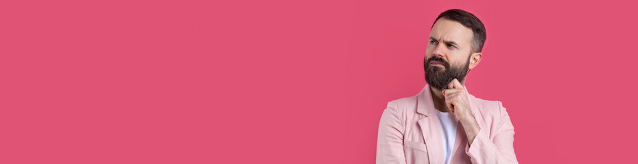 Obraz premium Handsome man with a beard in a pink jacket is thinking over an isolated red background.