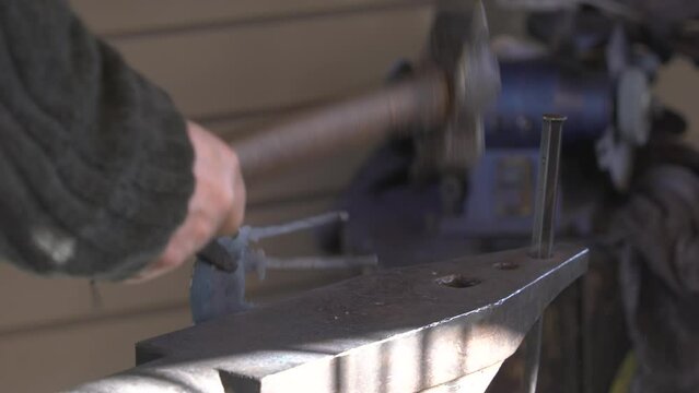 Anonymous blacksmith hits a hot metal workpiece with a hammer on an anvil with large tongs, close-up of tools and metal part. Rare professions, traditional blacksmithing