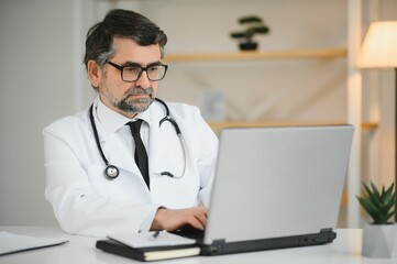 Portrait of senior doctor in white coat at workplace.