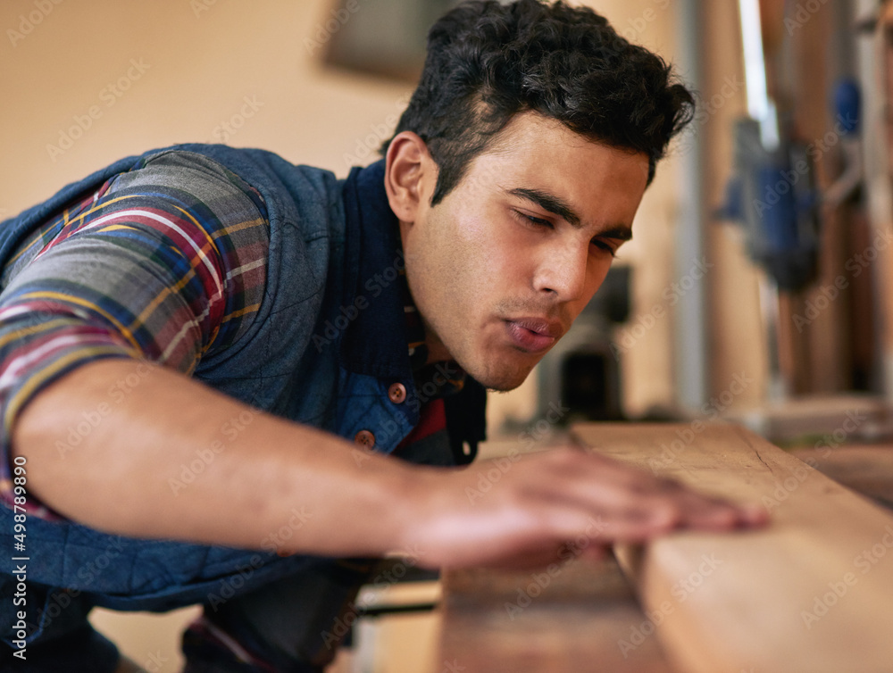 Poster he loves doing it himself. shot of a focused handyman examining a piece of wood while working in his
