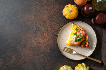A piece of frittata with pumpkin, bacon and ricotta in a ceramic plate on a dark culinary background. Traditional Italian delicious homemade egg dish on the kitchen table	