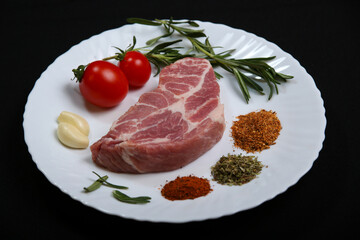 Fresh steak with spices and vegetables on a white plate and black background