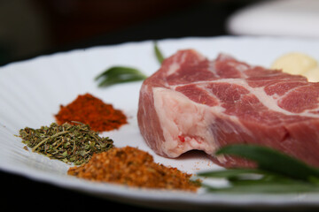 Fresh steak with spices and vegetables on a white plate and black background