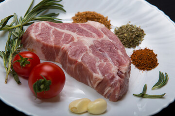 Fresh steak with spices and vegetables on a white plate and black background