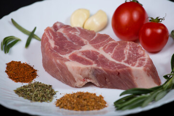 Fresh steak with spices and vegetables on a white plate and black background