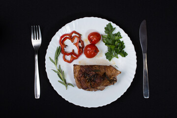 Fresh steak with spices and vegetables on a white plate and black background
