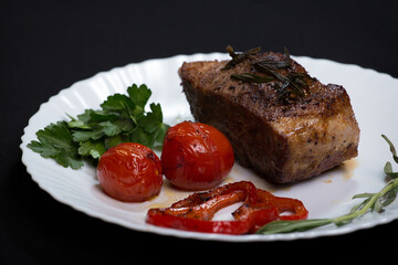 Fresh steak with spices and vegetables on a white plate and black background