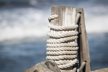 Rope on a weathered post on a dock next to the ocean