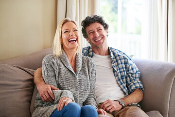I can always make her laugh. Shot of a mature couple laughing while relaxing on their sofa at home.