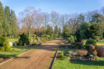 Spring sunny day at a beautiful and well-kept cemetery in Germany. The graves are decorated with candles and flowers. Cross in the background. The concept of the memorial day, the day of all saints. 