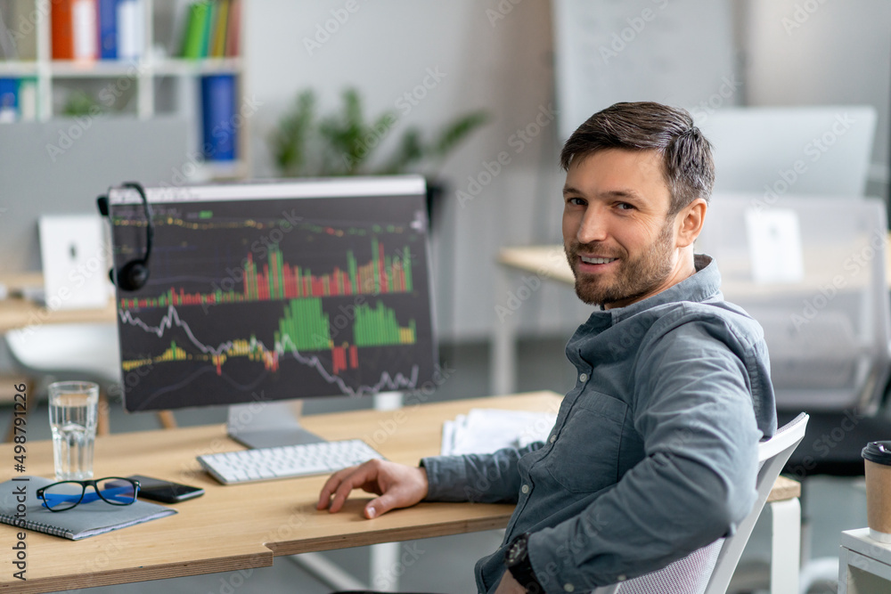 Poster Mature man working on computer in office and smiling at camera, monitor with graphics and charts