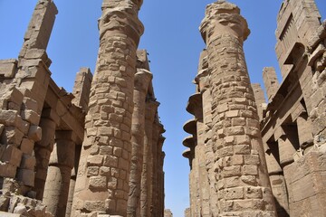 Stone pillars at the Karnak Temple in Luxor, Egypt, against blue sky.