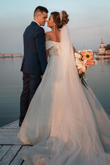 Loving couple at an international wedding at sunset. Beautiful sophisticated bride of Asian appearance. Stylish manly groom of European appearance. Mixed marriages