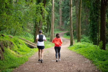 Back view of man and woman jogging in forest. Two sporty people in sportive clothes exercising outdoors. Sport, hobby concept