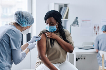 African young woman getting vaccination in arm with nurse during her visit at hospital