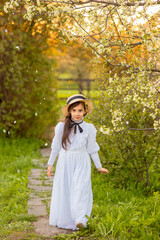 A pretty girl in a white dress and a hat walks under flowering trees in the spring