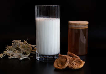 glass of milk, honey, medicinal herbal tea and dried fig on the black background