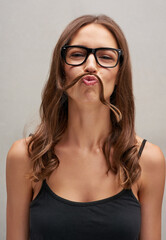 Looks like its Movember again. Studio portrait of an attractive young woman posing with her hair over her lip against a grey background.