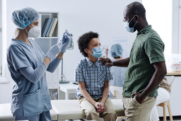 African father supporting his son while doctor preparing the syringe with medicine during...