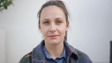 Portrait of beautiful blue eyed young caucasian woman looking at camera. Girl wearing denim shirt and knitted coat, grey wall background.