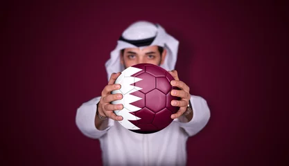 Fotobehang Arab man holding soccer ball in hand with Qatar flag standing on red background. © Moez