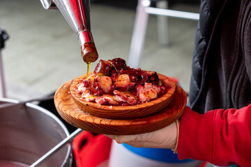 A man's hand pouring oil over a portion of octopus, prepared in the traditional Pulpo a feira...