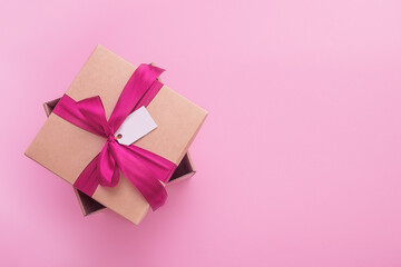 gift box with satin bow and tag on pink background with copy space