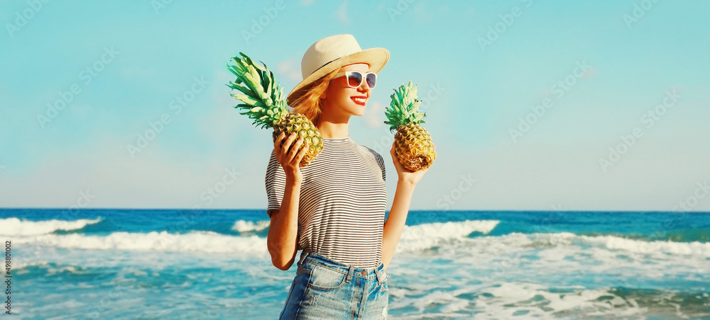 Wall mural portrait of happy smiling young woman holding two pineapples on the beach on sea background at summe