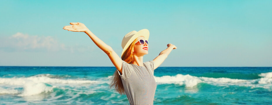 Happy smiling woman raising her hands up on the beach on sea background at summer day