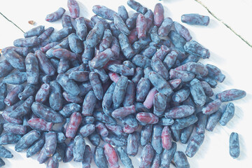 Blue fresh honeysuckle berries are scattered on a white table