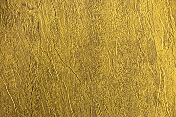 Golden wall with abstract spots as a background. Beautiful golden texture with patterns, decorative plaster. Modern bright wall painting in trendy shades, unusual spotted yellow and gold surface.