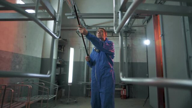 Worker in the paint shop of a metallurgical plant prepares a suspended product for painting and baking