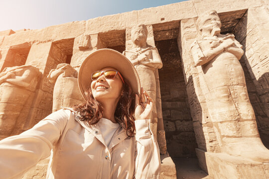 Travel blogger woman takes selfie photos among Pharaoh statues at the ruins of the famous Karnak temple in Luxor in Egypt