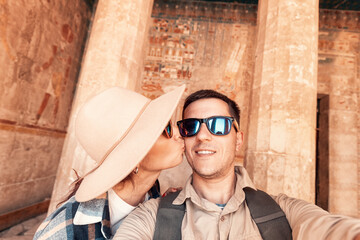 Happy traveler couple in love takes a selfie photo and kissing inside Hatshepsut Temple in Luxor during the honeymoon tour in Egypt