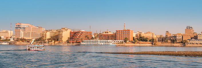 Panoramic view of traditional Egyptian ferry boats and cruise ships down the Nile with hotels of Luxor in the background