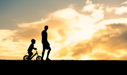Father son going for a walk riding bike at sunset. 