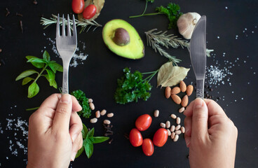 Hand holding fork knife agains assortment of healthy fresh raw food. Healthy diet concept. 