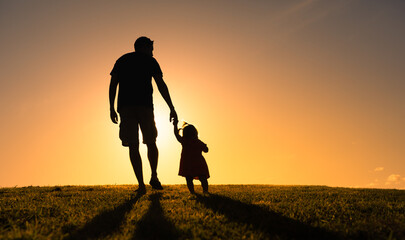 Silhouette of father holding his child's hand walking into the sunset. Fatherhood, parenting concept.  - obrazy, fototapety, plakaty