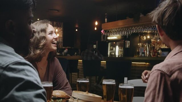 Multiracial woman joins group of friends at restaurant for dinner and drinks. She greets and hugs her friends when she arrives.