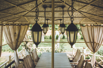 Beautiful vintage lamps. Wooden white gazebo in the summer garden. White garden furniture. Rest and relaxation in the private garden