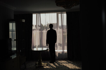 Fototapeta na wymiar Dark silhouette of man looking through a window at a big city.