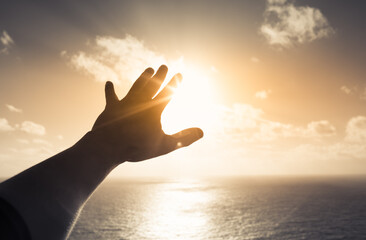 hand reaching out to the sky at dawn