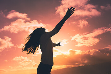 Woman looking up to the sunrise sky with open arms. People with feelings of positivity, and happy state of mind